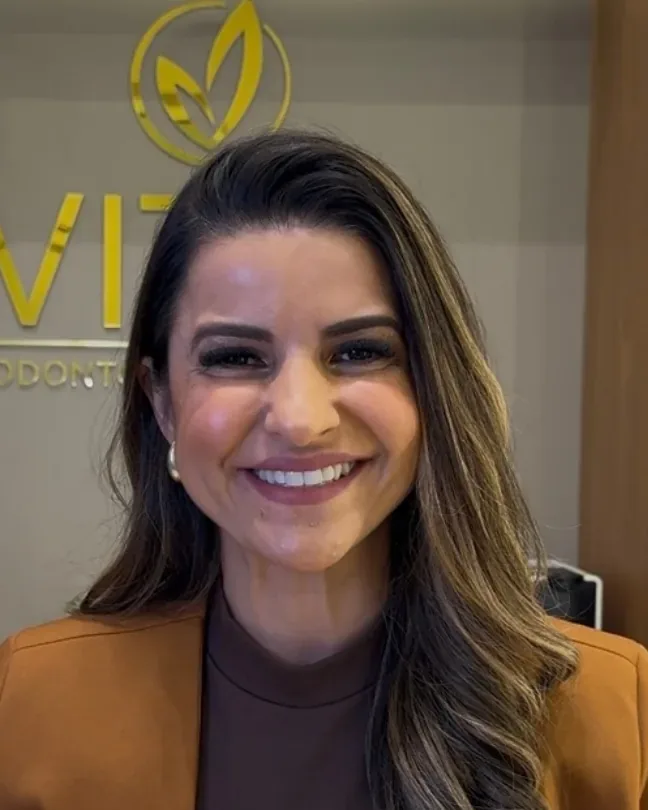 Dra. Tatiane Mota, ortodontista da Vitta, na recepção diante do logo dourado